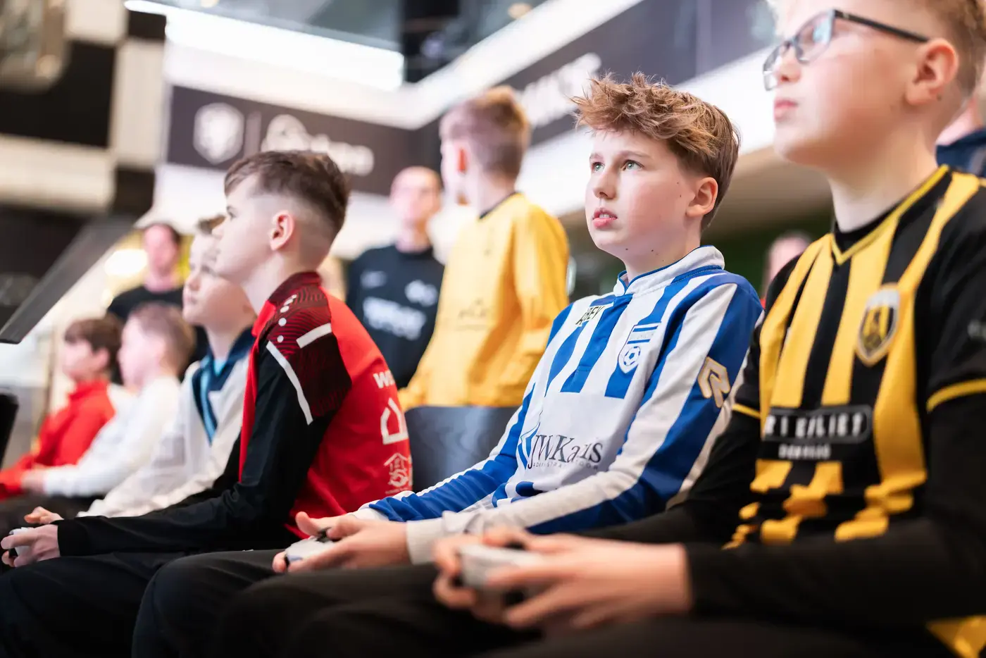 Geconcentreerde jongens in voetbalshirts spelen FIFA met controllers tijdens een esports toernooi