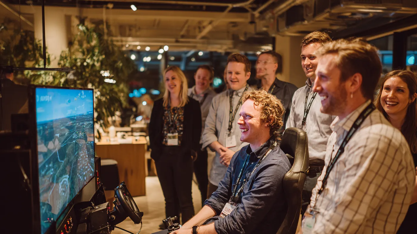 Groep nieuwsgierige professionals staat rond een vluchtsimulator met groot scherm tijdens een corporate event